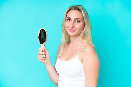 Young caucasian woman with hair comb isolated on blue background smiling a lot