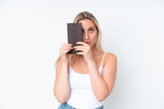 Young caucasian woman isolated on white background taking a chocolate tablet and surprised