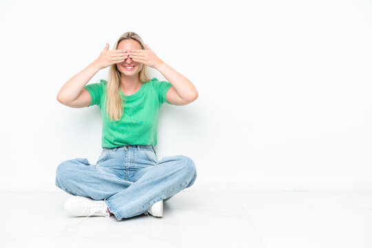 Young caucasian woman sitting on the floor isolated on white background covering eyes by hands