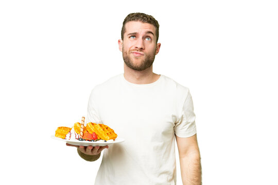 Young handsome blonde man holding waffles over isolated chroma key background and looking up