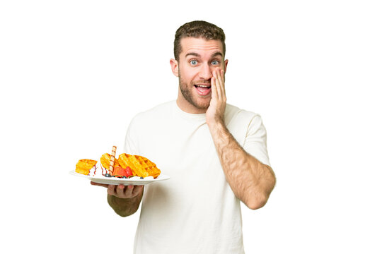 Young handsome blonde man holding waffles over isolated chroma key background with surprise and shocked facial expression