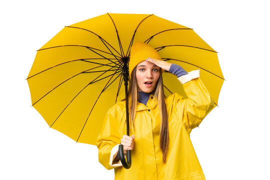 Teenager girl with rainproof coat and umbrella over isolated chroma key background doing surprise gesture while looking to the side