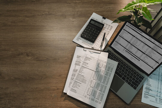 Tax preparation workspace with tax worksheet on laptop, calculator, financial reports and wide copy space for accounting, tax season, bookkeeping, planning.