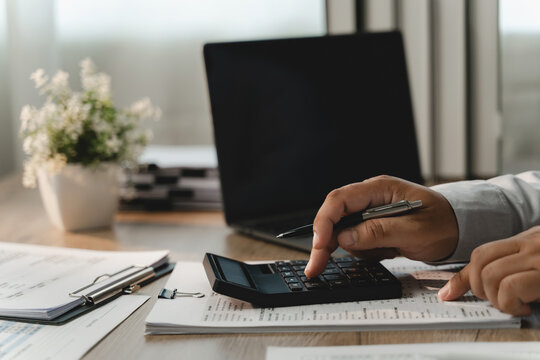 Businessman reviewing financial documents with calculator, pen, laptop for corporate budgeting, accounting analysis, revenue planning, expense control, profit strategy in modern office.