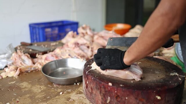 Close-up of a vendor cutting and butchering raw chicken breast meat on a wooden chopping block with a cleaver at Xom Moi Market in Nha Trang, Vietnam. Commercial food supply and retail trade concept.