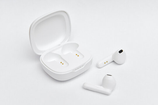 Modern bluetooth earphones out of charging case on white background