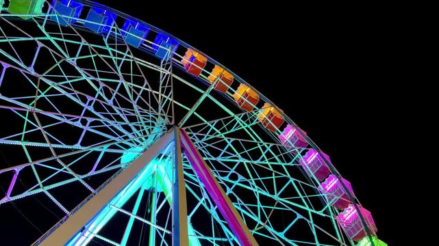 Bright colors illuminate a Ferris wheel at a fair in the city. People enjoy rides and attractions. Nighttime brings a lively atmosphere. Guests smile and take photos.