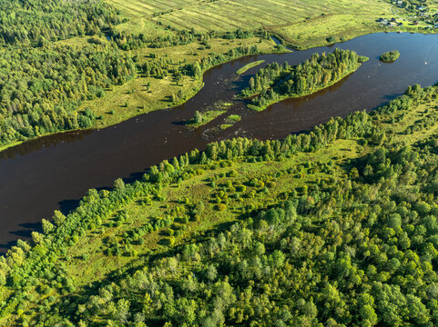 Aerial view of a winding river meandering through green taiga forest and fields near Kindasovo village in Karelia, Russia