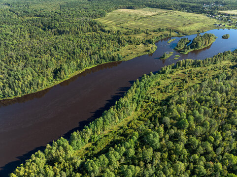 Aerial view of a winding river meandering through green taiga forest and fields near Kindasovo village in Karelia, Russia