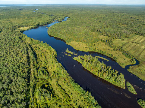 Aerial view of a winding river meandering through green taiga forest and fields near Kindasovo village in Karelia, Russia