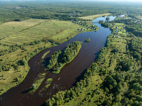 Aerial view of a winding river meandering through green taiga forest and fields near Kindasovo village in Karelia, Russia
