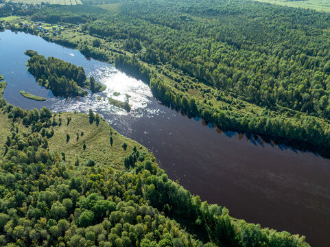 Aerial view of a winding river meandering through green taiga forest and fields near Kindasovo village in Karelia, Russia