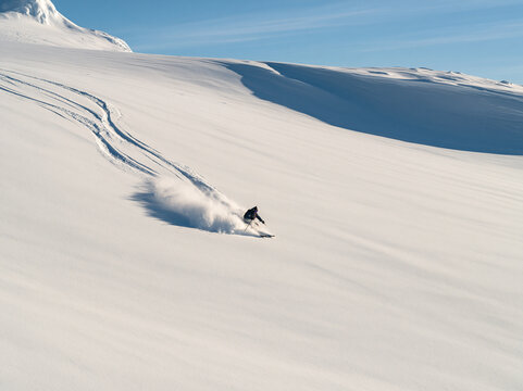 Distant view of a skier freeriding on a vast untracked snow mountain slope under a clear blue sky