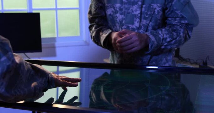 Two uniformed military personnel use a large touchscreen map table in a dim command center, planning a tactical operation with digital navigation tools.