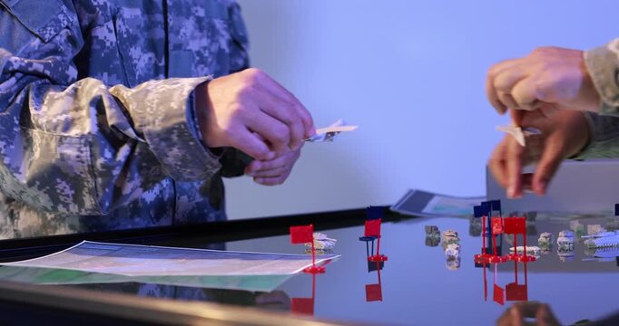 Close view of military personnel in camouflage uniforms moving markers on a tabletop map during a tactical planning exercise.