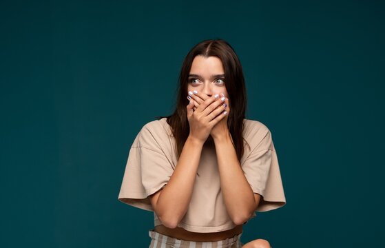Young woman covering mouth with hands, feeling fear, expressing shock, keeping a secret, feeling afraid to speak