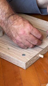close up of man holding hex key fastening threaded insert nuts screwing into wood assembling flat-pack furniture