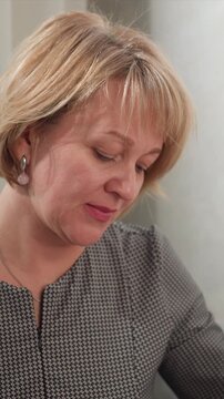 Close up of woman with short blonde hair wearing earrings and holding object in soft lighting. Her clothing features black houndstooth pattern fine details include her necklace and texture