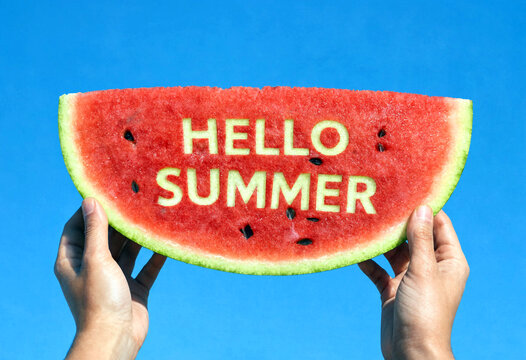 Hands holding a large watermelon slice with hello summer text against clear blue sky