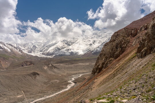 Achik-Tash river valley below snow covered mountains peaks and beautiful white clouds in summer