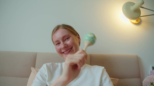 From baby perspective, mother guides moving rattle across view during home play. Visual motion supports focus, tracking, sensory discovery, anticipation, trust, and lively parent child interaction.