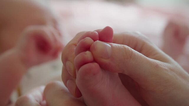 Close-up focuses on newborn toes during gentle massage by mother. Detailed contact reveals soft pressure, tactile awareness, relaxation, comfort, trust, and nurturing maternal care.
