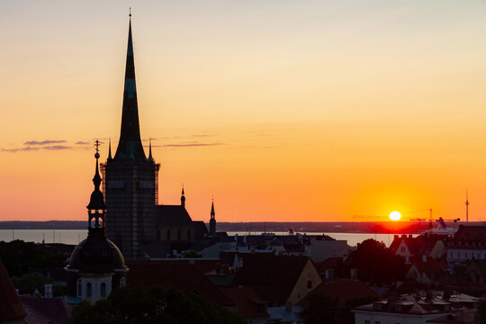 Stunning sunrise over the skyline of the old town of Tallinn, Estonia, featuring the silhouette of St. Olaf's Church spire and other historic rooftops against a glowing morning sky.