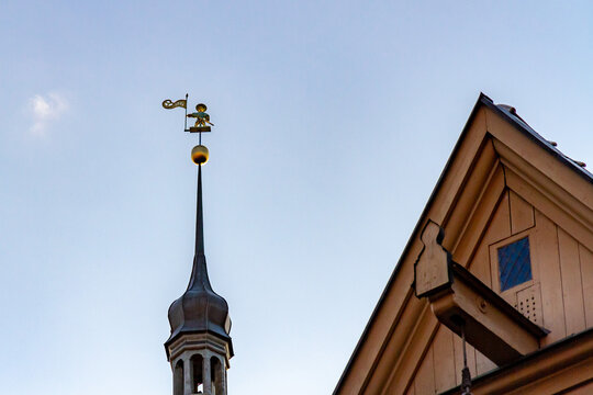 Early morning sunlight illuminating Vana Toomas (Old Thomas), the famous historic weather vane atop Tallinn Town Hall spire, next to a wooden gable roof in the old town of Tallinn, Estonia.