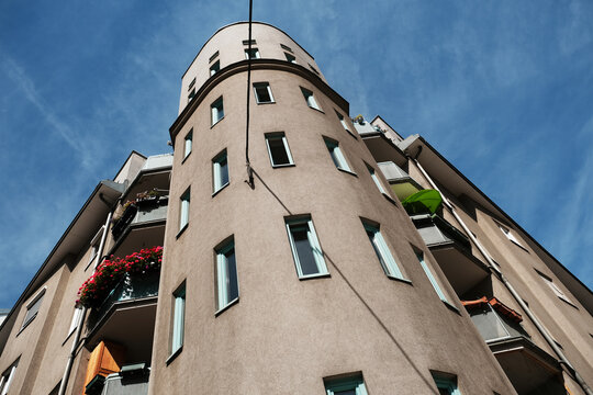 A contemporary apartment building featuring a unique curved corner facade, windows, and balconies with red flowers under a clear blue sky in Vienna, Austria.