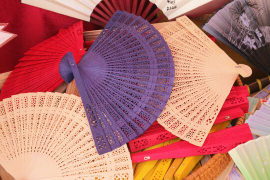 Asian folding hand fans with carved lace pattern texture, colorful wooden sandalwood fans on tourist souvenir market display, Vietnam