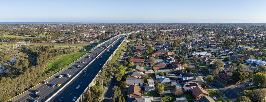 Aerial&nbsp;panorama view of Princes Freeway traffic bordering suburban residential housing, green reserves, and a railway line in Laverton, Melbourne, Australia. Traffic parallel to rail infrastructure