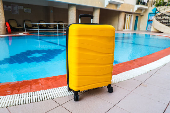 A bright travel suitcase stands next to a small swimming pool, summer vacation concept.