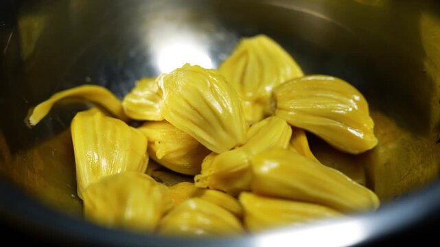 Fresh yellow jackfruit pods in a metal bowl, close-up of peeled tropical fruit ready to eat.