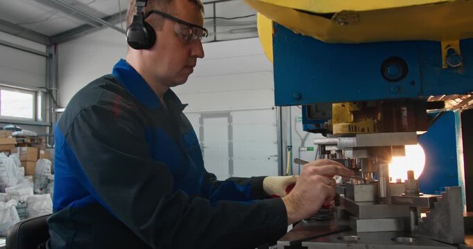 Experienced machine operator working with industrial press equipment. Skilled labor in manufacturing workshop