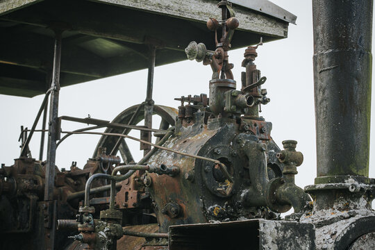 Vintage steam engine machinery with intricate metal components and pipes, showcasing rust and wear, set against a cloudy sky in an outdoor environment