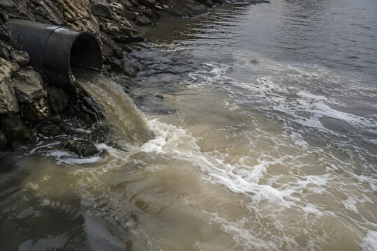 Water flows from a pipe into a river at a rocky bank