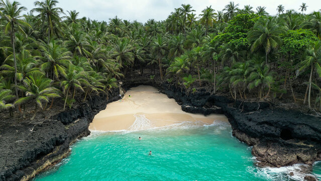 Couple swimming in the turquoise waters of Praia Bateria, Ilh&eacute;u das Rolas, S&atilde;o Tom&eacute; and Pr&iacute;ncipe, surrounded by volcanic cliffs, white sand, and coconut palms.Africa