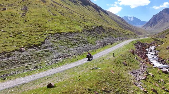 Man rides sport enduro motorcycle by the mountain road in narrow valley between snow peaked mountains. Scenic landscape, vivid colors. Outdoor activity and motorcycling concept.