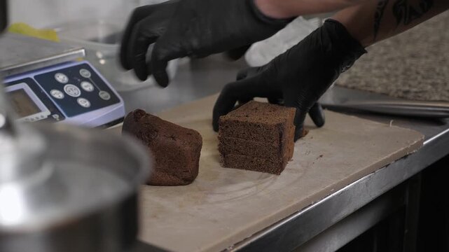 Close-up of the chef slicing black bread with a knife to make deep-fried croutons in the restaurant kitchen. The process of making croutons involves garlic, beer, and fast food.