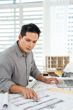 Young asian civil engineer studying a blueprint floor plan and  working with documents, drawings and building models.