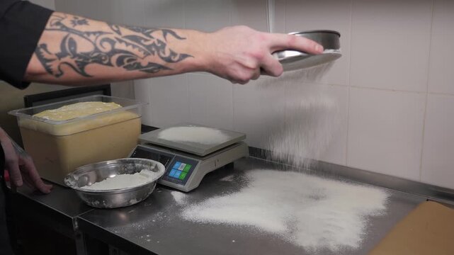 The chef of the restaurant sifts flour on the dough table, weighing the dough for burger buns in the restaurant kitchen.