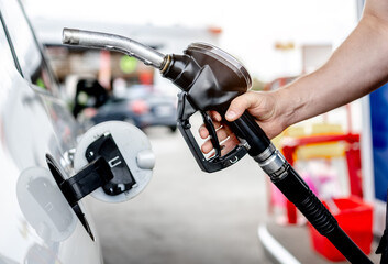 Naklejka premium Person filling up white car fuel tank at local gas station