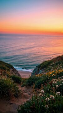 Scenic cliffside dirt trail descending to a sandy beach and ocean under a dramatic vibrant orange sunset sky