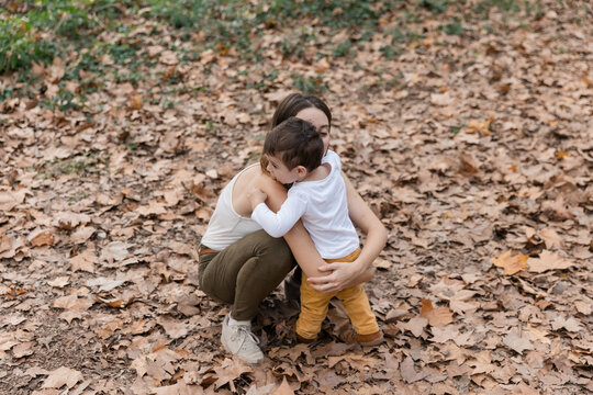 Mother hugging child on autumn dried leaves