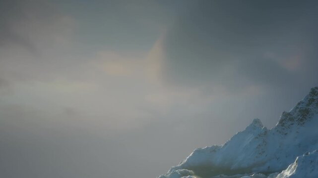 Snow covers the peak of a mountain with clouds surrounding it. The scene captures the quietness of evening. Light reflects off the snow and clouds creating a unique view.