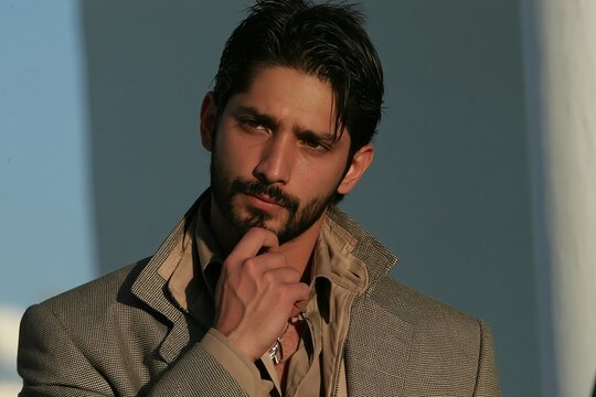 Thoughtful handsome man with dark hair and beard posing outdoors in patterned jacket