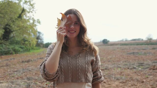 Happy young woman hiding eye with an autumn leaf