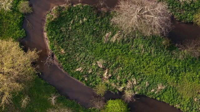 Close top down view of winding river bend and green riverbank in rural Normandy. Drone footage of rural landscape design and waterway corridor