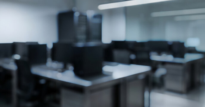 A blurred view of a modern office interior featuring multiple computer desks and technology. The ambiance suggests a quiet, professional workspace.