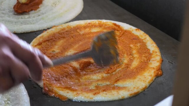 spicy masala being spread over crispy benne dosa on hot griddle